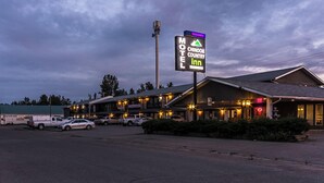 A motel with a signboard, multiple parked cars, and a building with lights on. - Chinook Country Inn (Sundre)