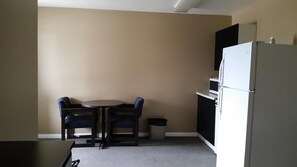 A small kitchenette with a refrigerator, microwave, and a trash can. There is a round table with two chairs.