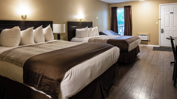 A hotel room with two beds, a door, a window with curtains, and a wall-mounted light fixture. - Chinook Country Inn (Sundre)