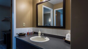 A bathroom with a large mirror, a sink, and toiletries on the counter. - Chinook Country Inn (Sundre)
