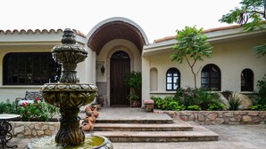 A courtyard with a fountain, steps leading to a door, and a stone wall. - Hacienda Edith (Cabo San Lucas)