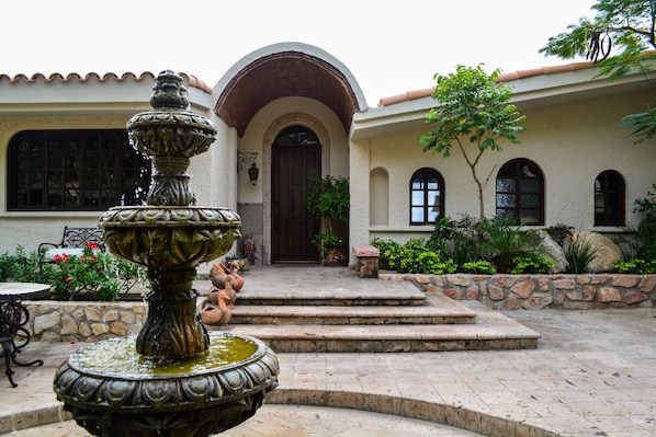 A courtyard with a fountain, steps leading to a door, and a stone wall.