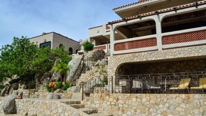 A pool area with stone steps leading to a bar area, surrounded by greenery and a stone wall. - Hacienda Edith (Cabo San Lucas)