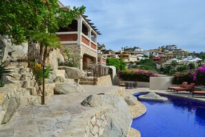 A stone staircase leading to a pool area with lounge chairs and a view of a hillside residential area.