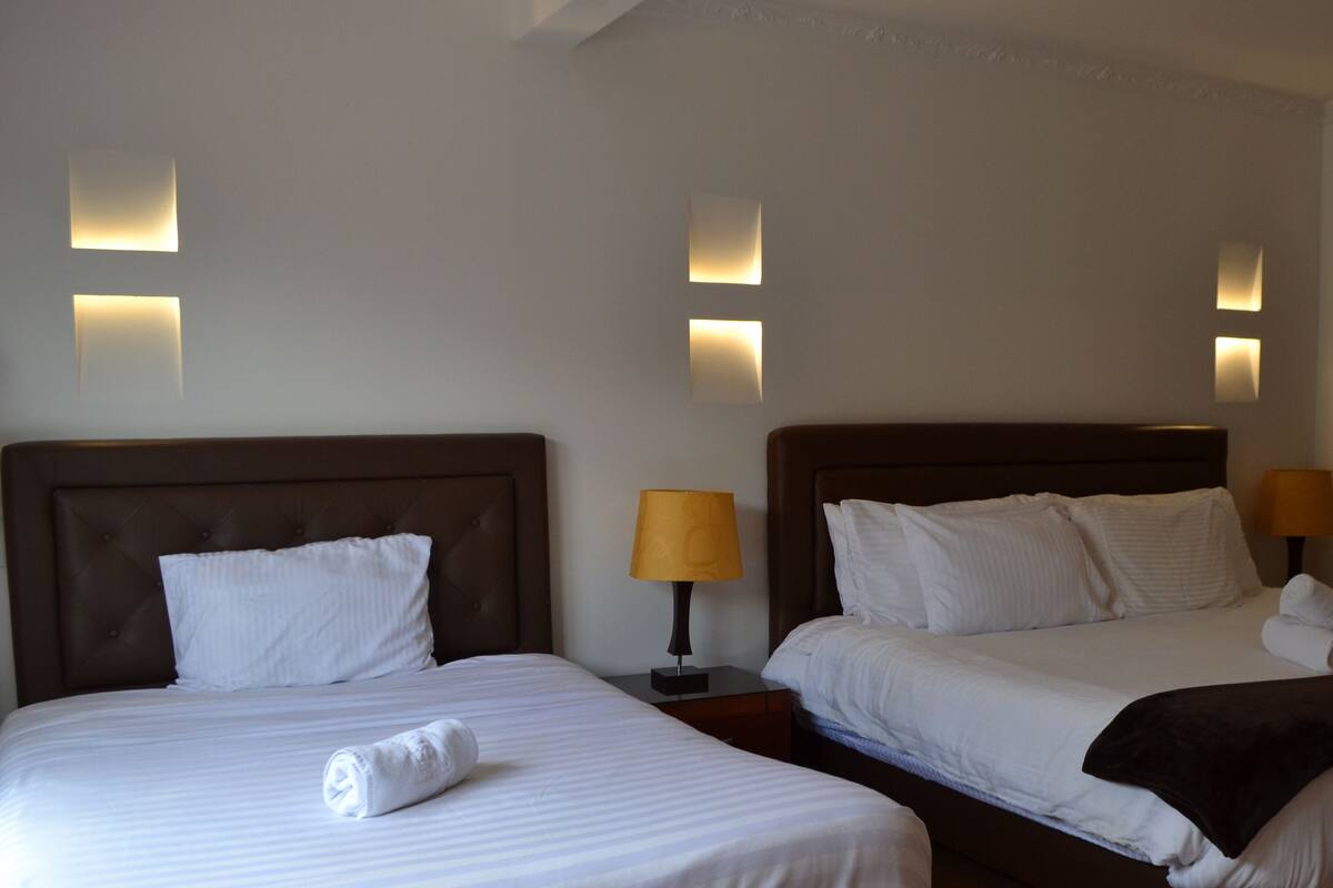 Une chambre d’hôtel avec deux lits, chacun doté d’une tête de lit, d’une table de chevet avec une lampe et d’un éclairage mural.