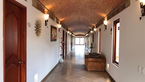 Um corredor longo e estreito com portas e paredes de madeira, decorado com arandelas e obras de arte.