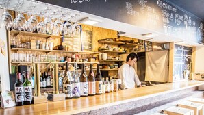 A bar area with a counter displaying various bottles, glasses, and a chalkboard menu. - BACCHUS Kofu Guest House - Hostel (Kofu)