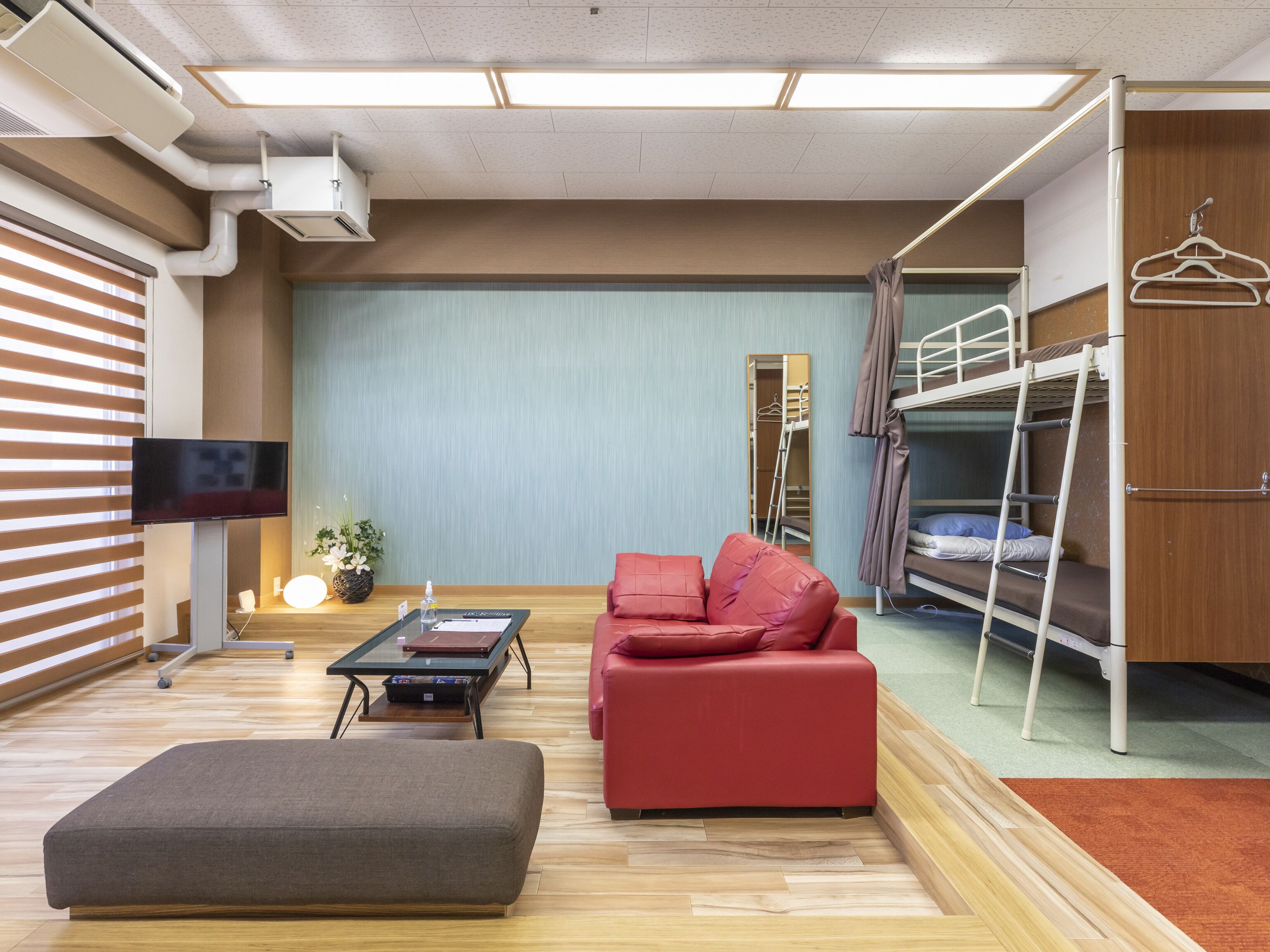 A compact hotel room with a sofa, a small table, a TV, a bunk bed, and a mirror.