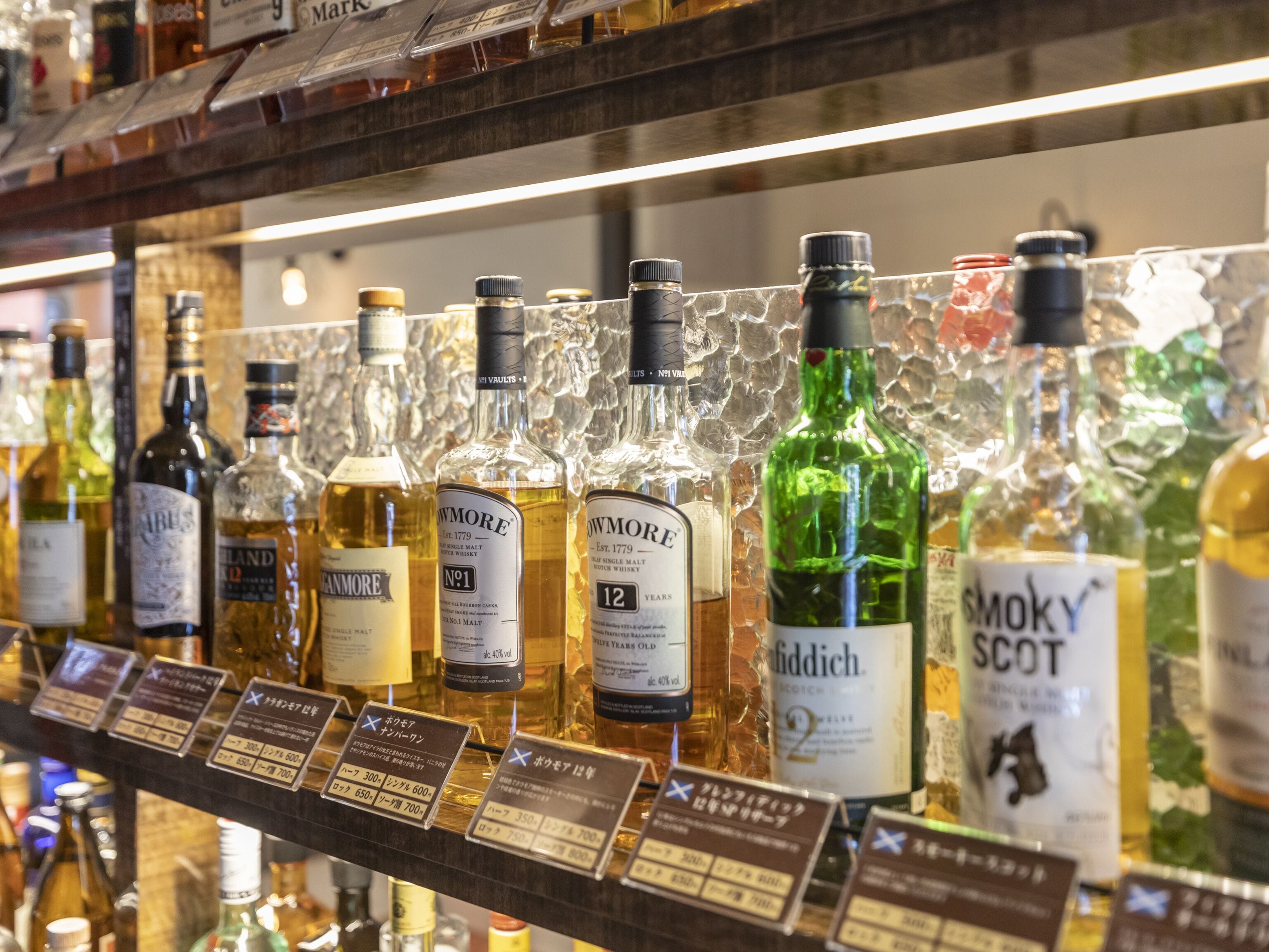 A selection of whisky bottles on a shelf with price tags.