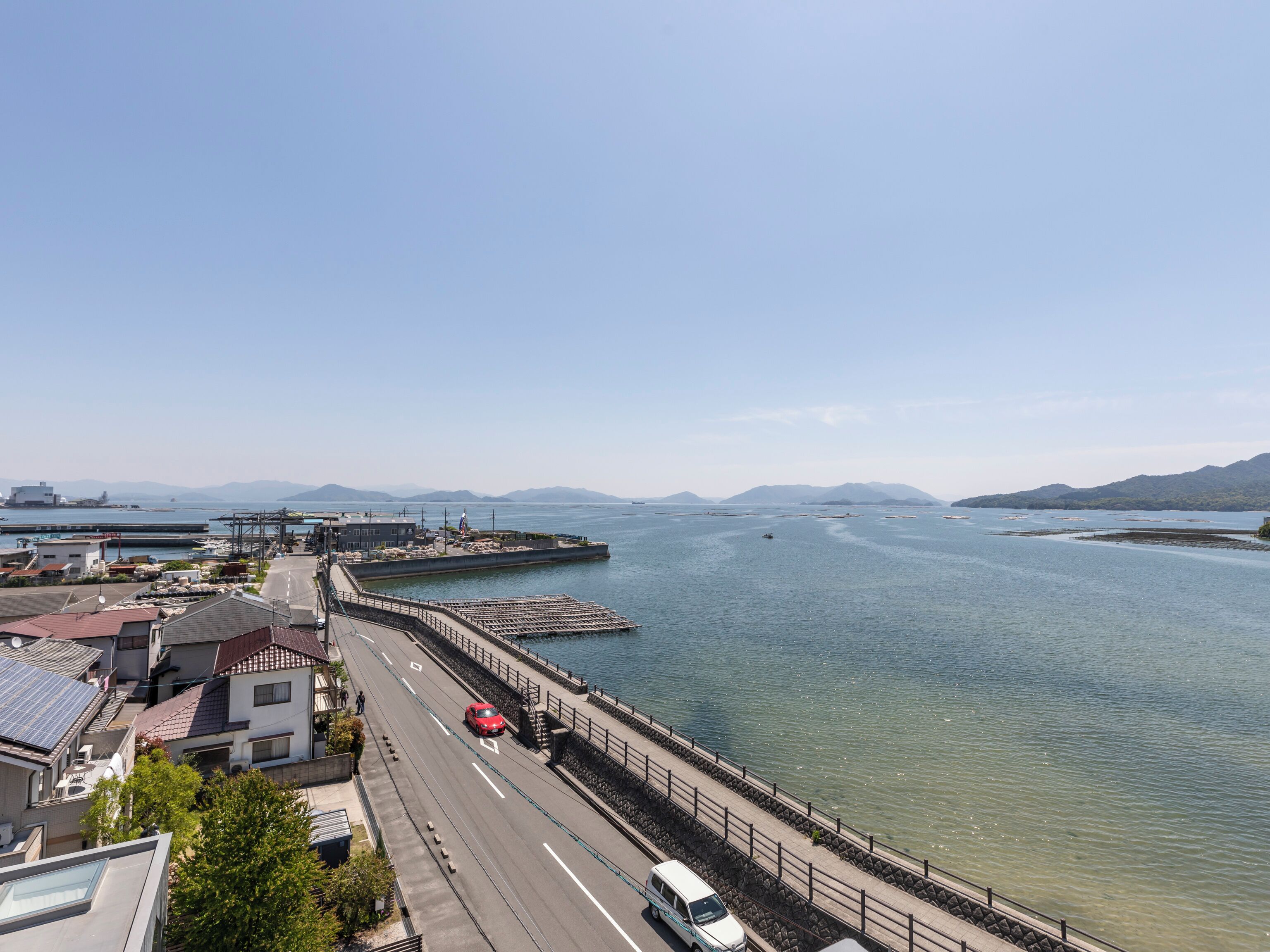 A coastal road with a bridge, a marina, and distant mountains.