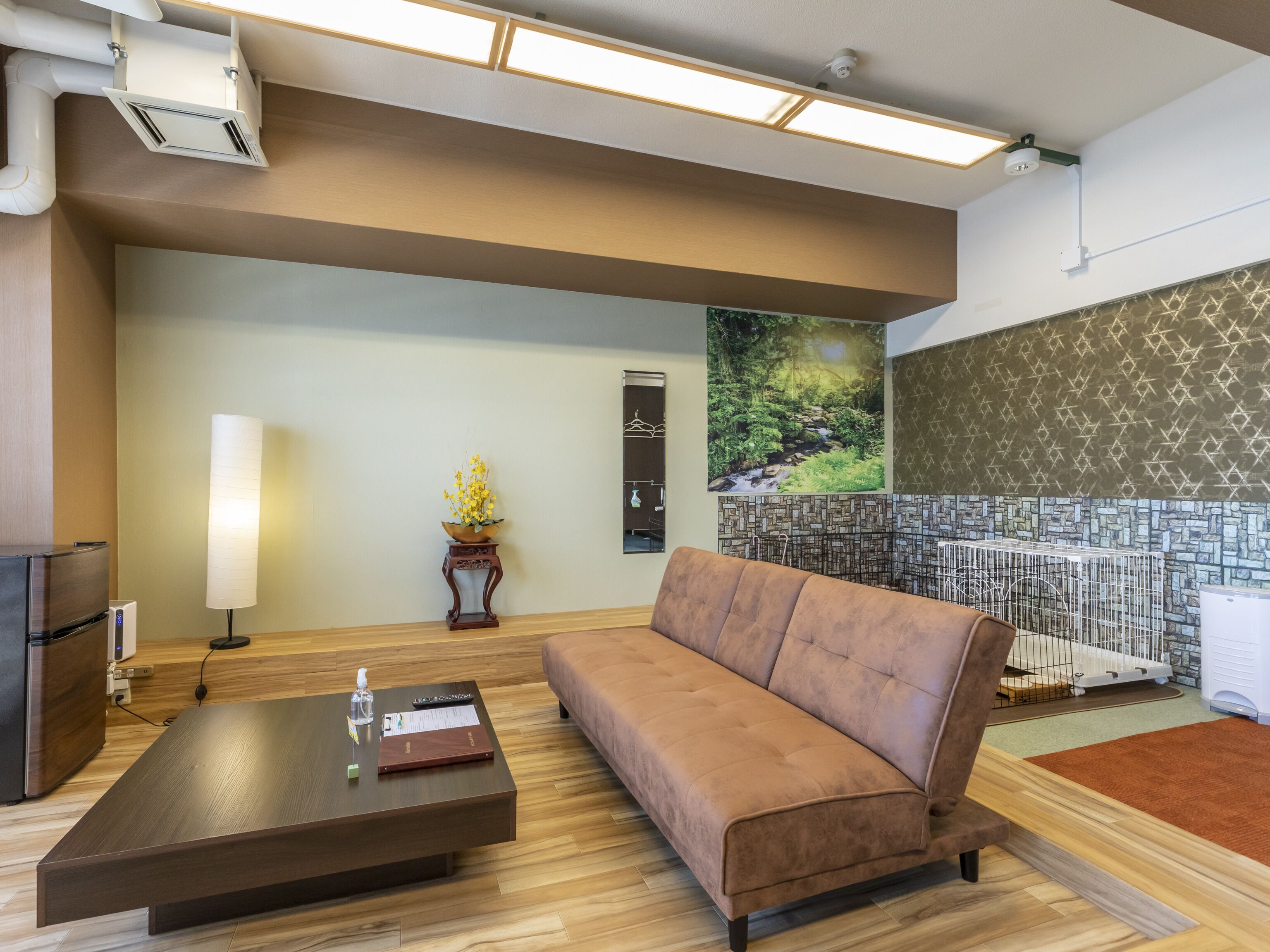A modern hotel lobby with a sofa, a coffee table, a lamp, and a painting of a forest scene.