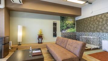 A modern hotel lobby with a sofa, a coffee table, a lamp, and a painting of a forest scene.