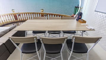 Et konferencemødebord med seks stole, et hvidt gelænder og udsigt til en strand med overvandsbungalows.