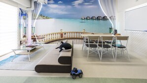 A room with a ceiling mural of a beach scene, a dining area with chairs and a table, and a sofa with a toy dog. - OMOTENASHI Hostel Miyajima (Hatsukaichi)