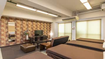 A hotel room with a flat-screen TV, a sofa, a small table, and a decorative plant.