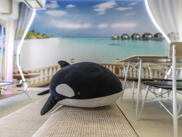 Un peluche sobre una superficie texturizada, con un fondo desenfocado que muestra una masa de agua y bungalows sobre el agua.