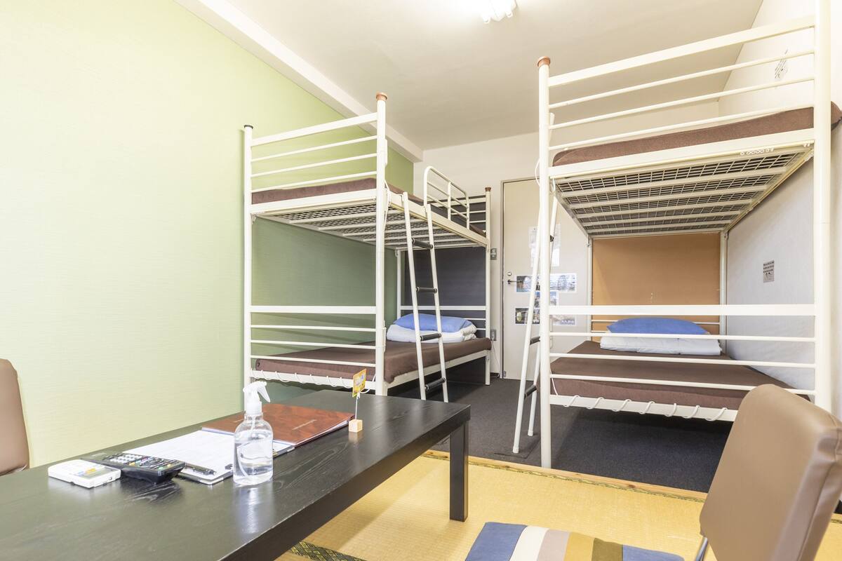 A dormitory room with bunk beds, a desk, and a chair.