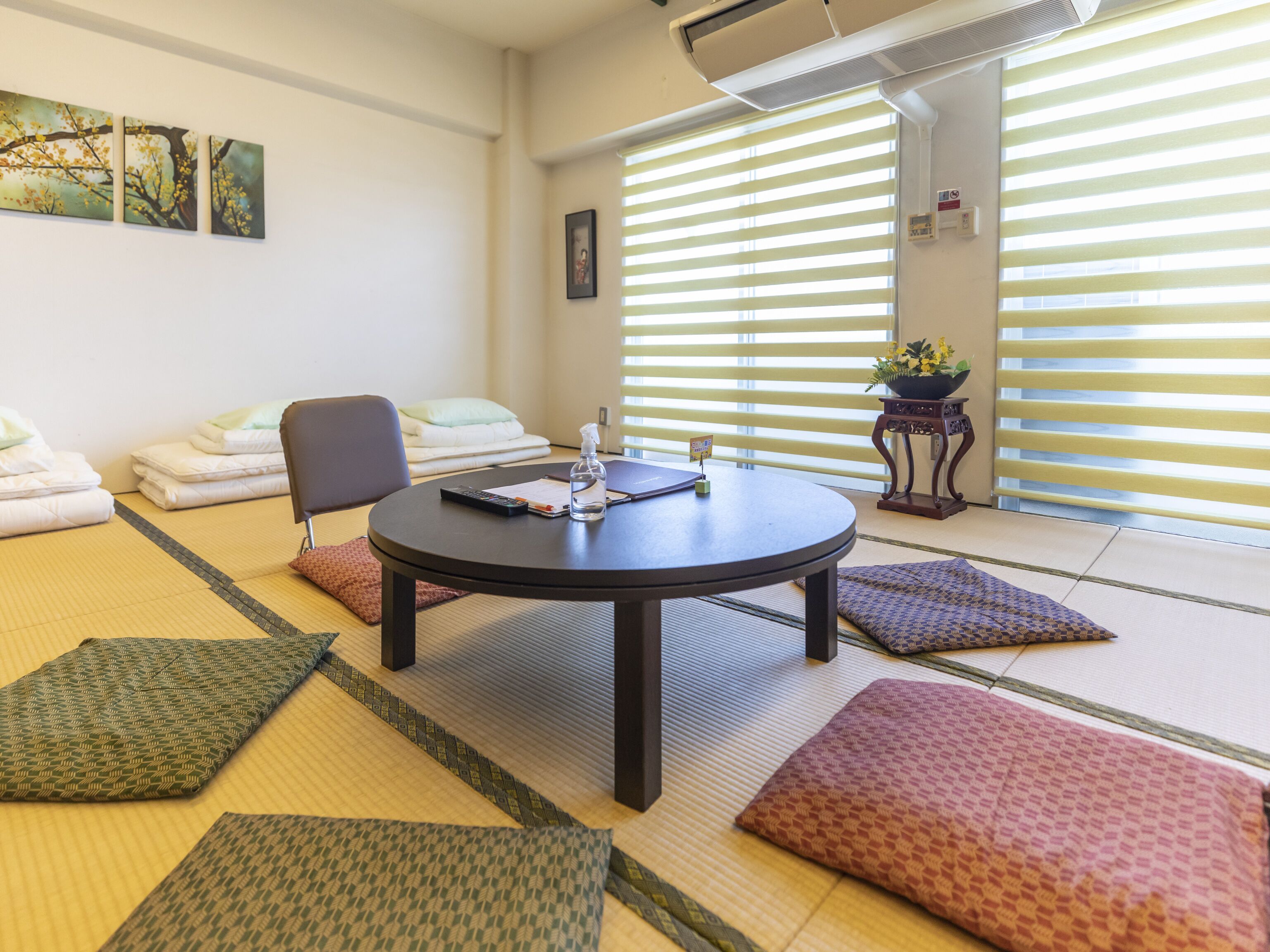 A room with tatami mats, a round table with a remote control, a water bottle, and a small plant.