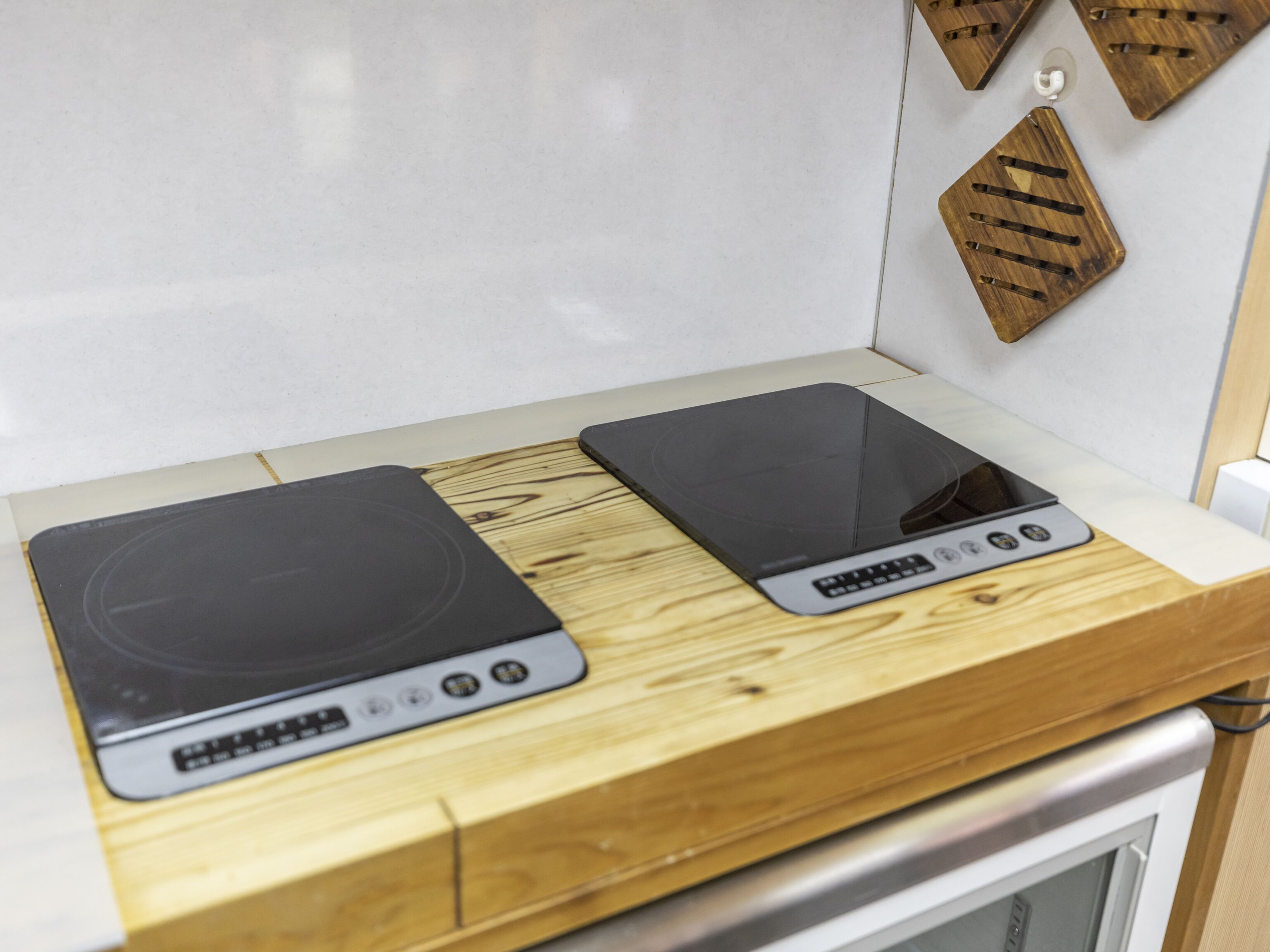 Eine Küche mit zwei Induktionskochfeldern auf einer Holzausziehtafel, einer weißen Fliesenspiegel und einem Edelstahlbackofen darunter.