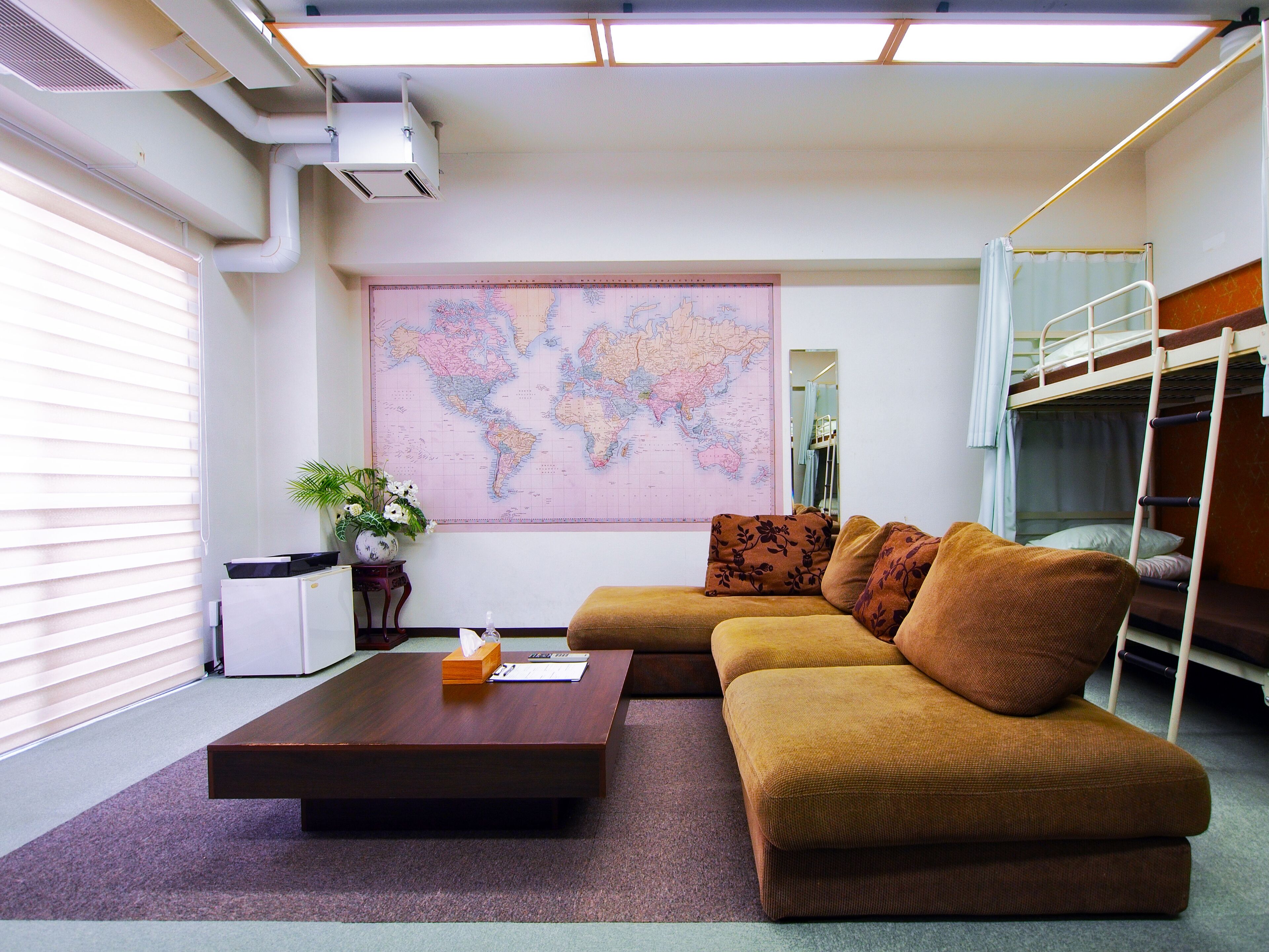 A room with a sofa, a coffee table, a world map on the wall, a bunk bed, and a window with blinds.