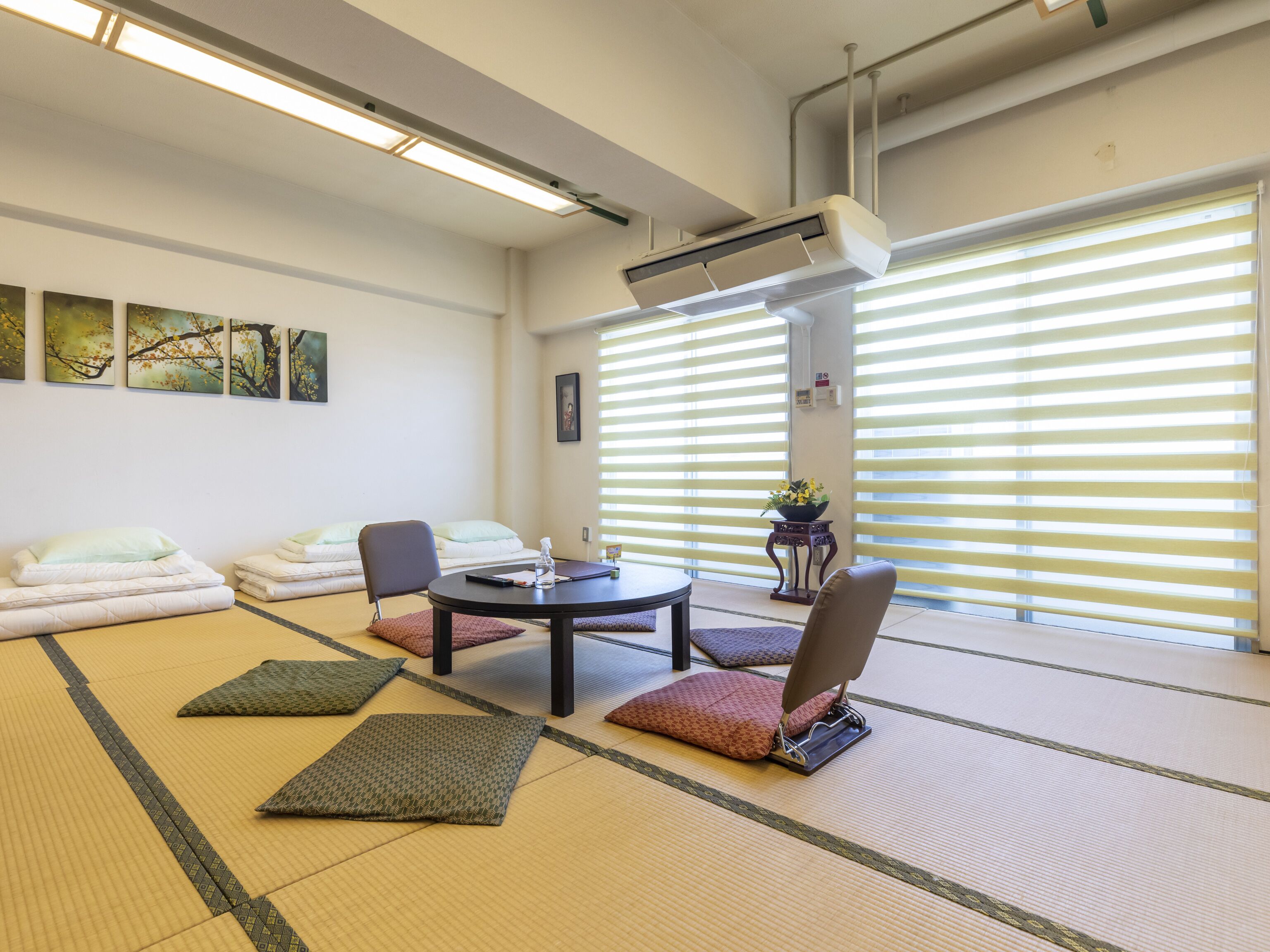 Una habitación con suelo y esteras de tatami, una mesa baja, sillas y una futón.