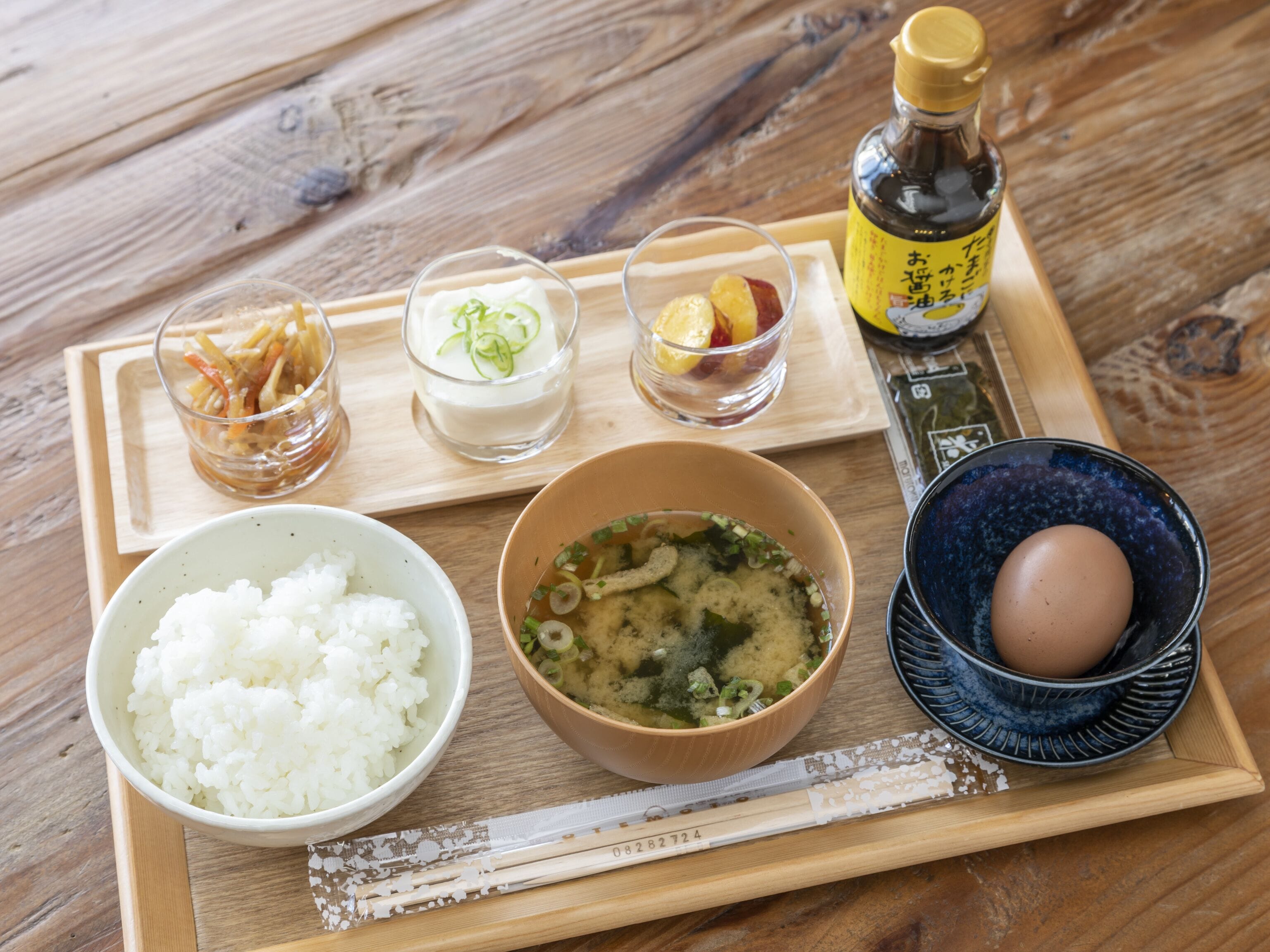 Ein Holztablett mit verschiedenen Speisen, darunter Reis, Suppe und eine Sojasauce.