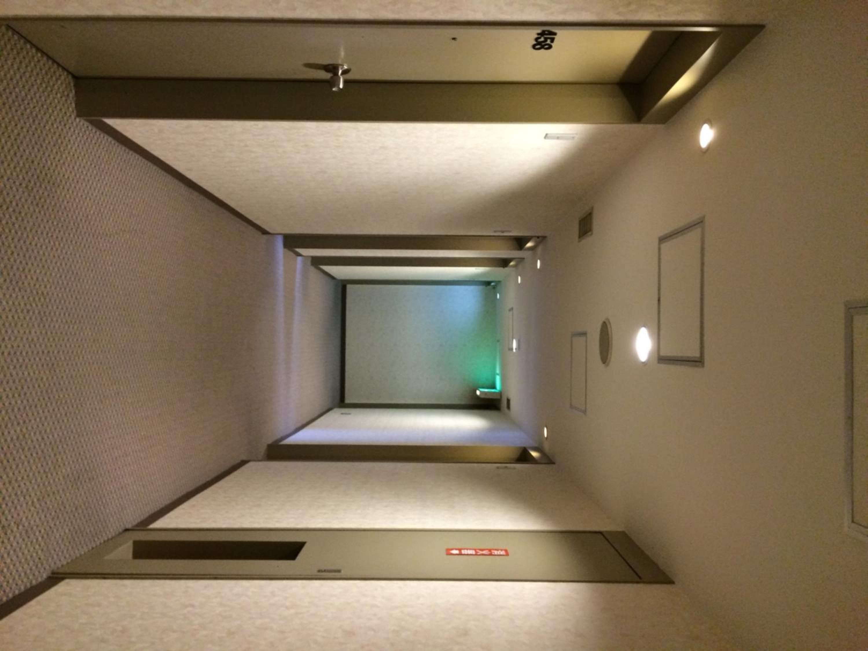 A narrow hallway with a carpeted floor, a door at the end, and a small vent on the wall.