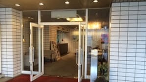 A hotel entrance with a glass door, a reception desk, and a tiled wall. - Sky Hotel Uozu Annex (Uozu)