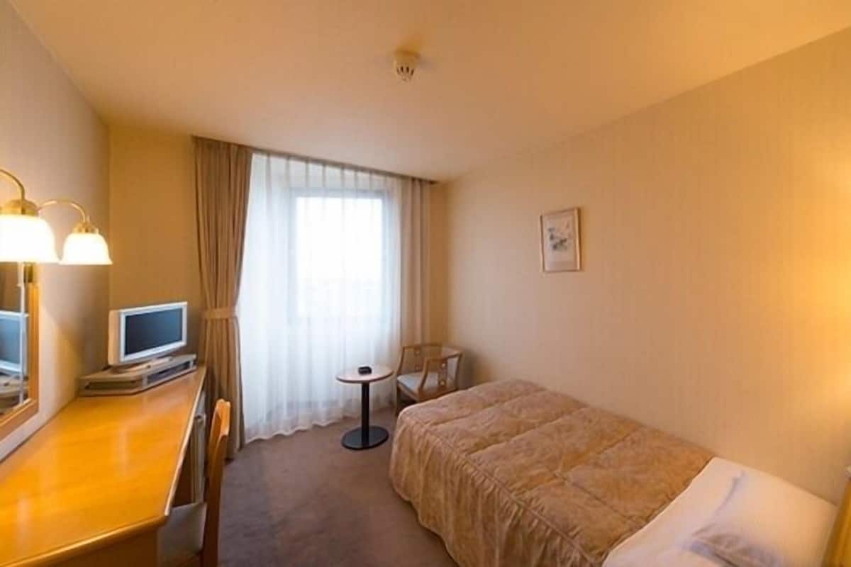 Quarto de hotel com cama, secretária, computador, cadeira, mesinha e abajur.