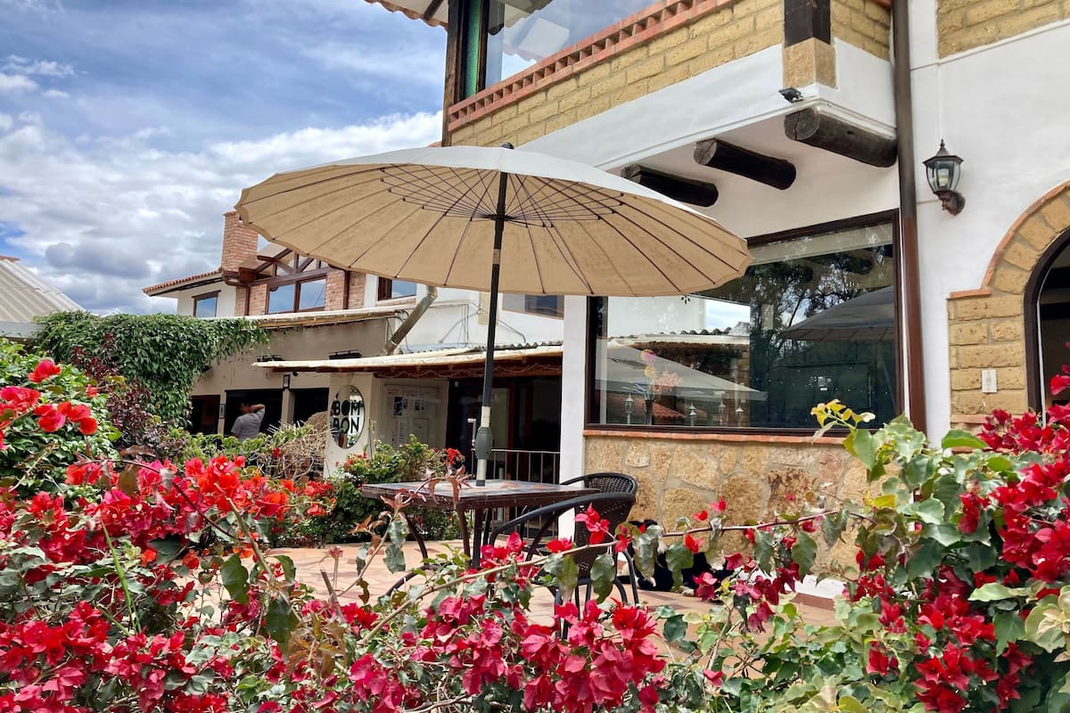 A building with a patio area featuring a table and chairs, surrounded by red flowers and greenery.