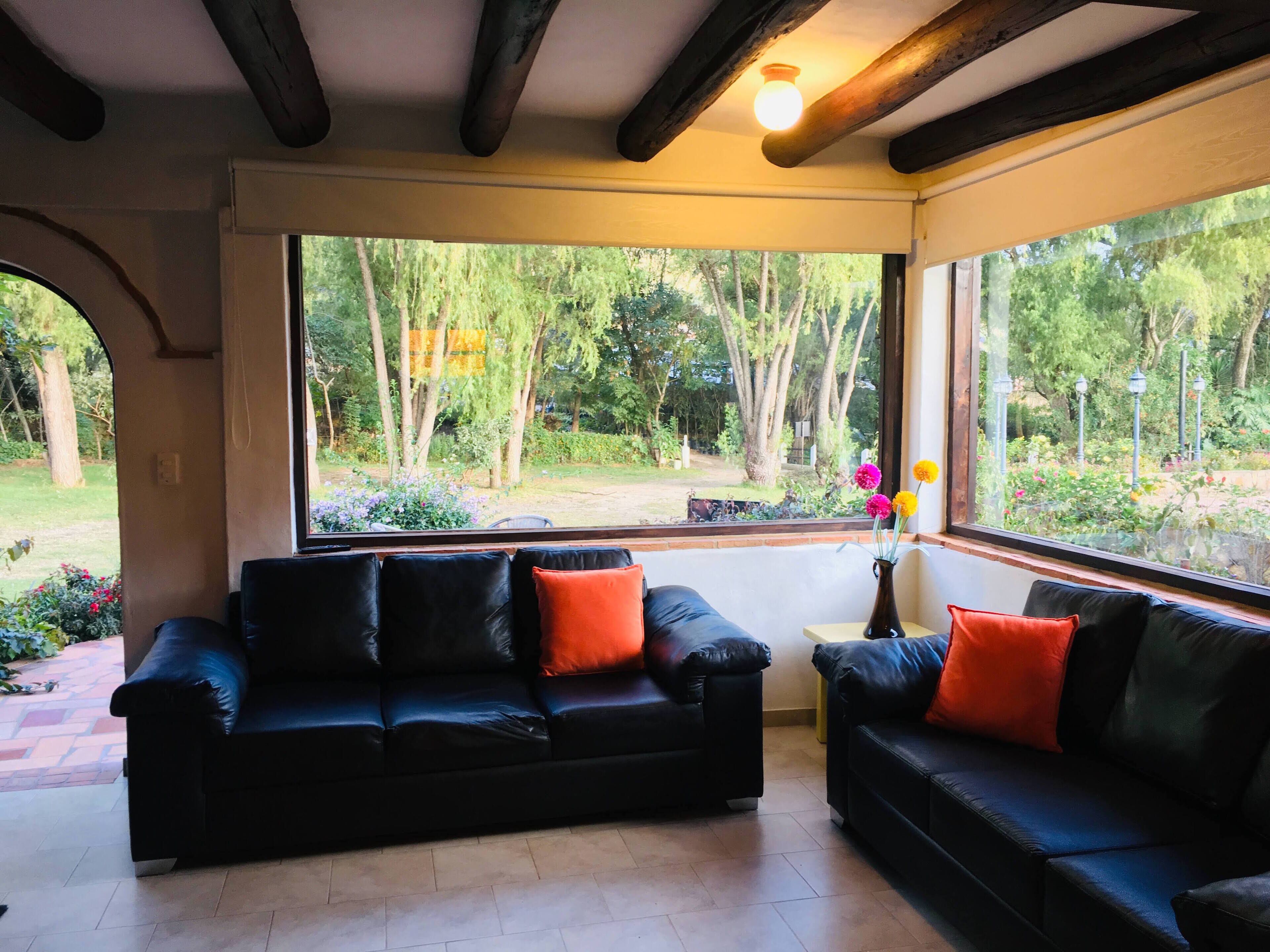 Una habitación con un sofá de cuero negro, una mesita con un jarrón de flores y vistas a un jardín a través de amplios ventanales.