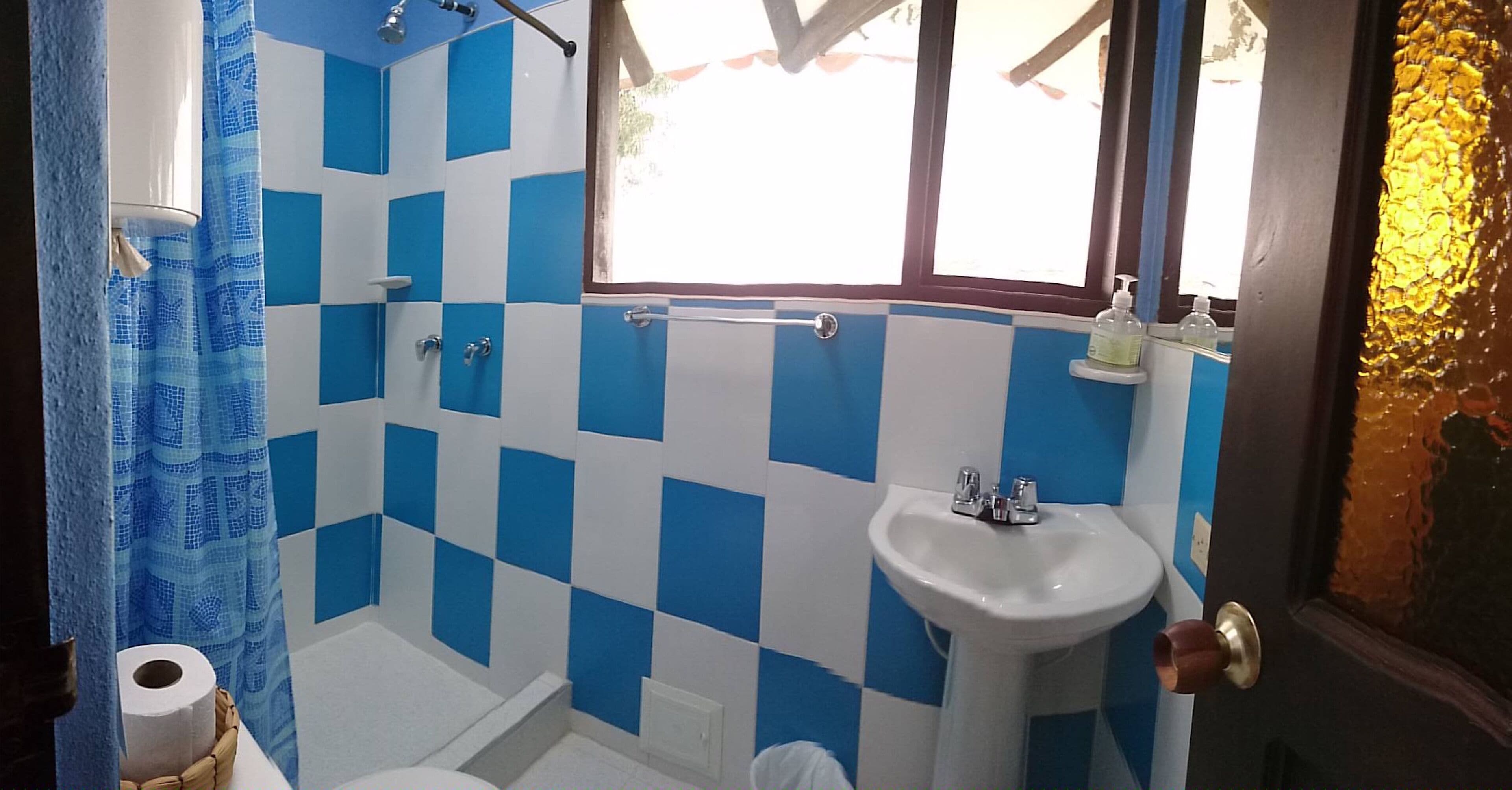 Un baño con pared de azulejos blancos y azules formando un diseño a cuadros, un lavabo blanco y una zona de ducha.