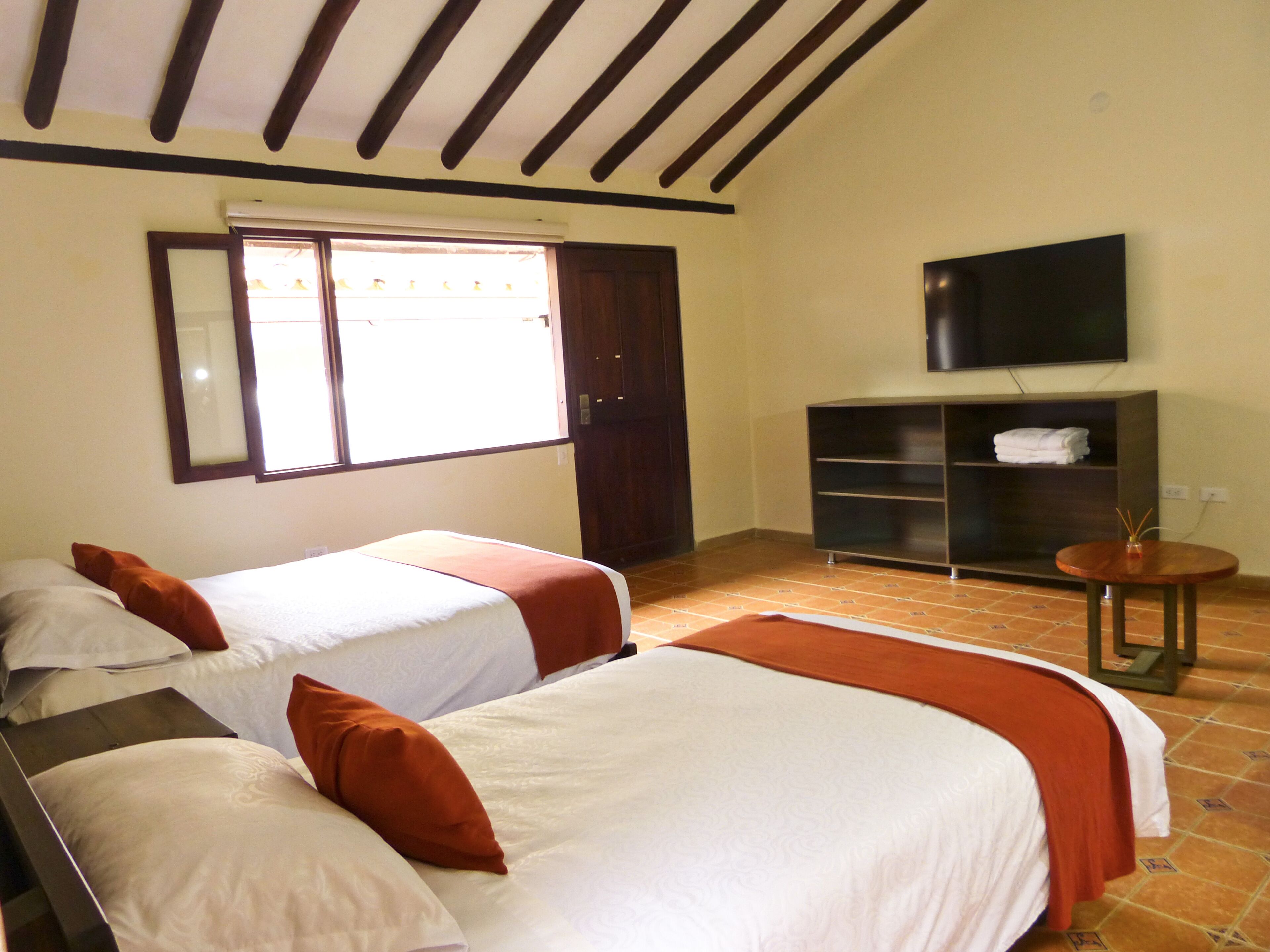 Un dormitorio con dos camas, un televisor, una mesita y una ventana.