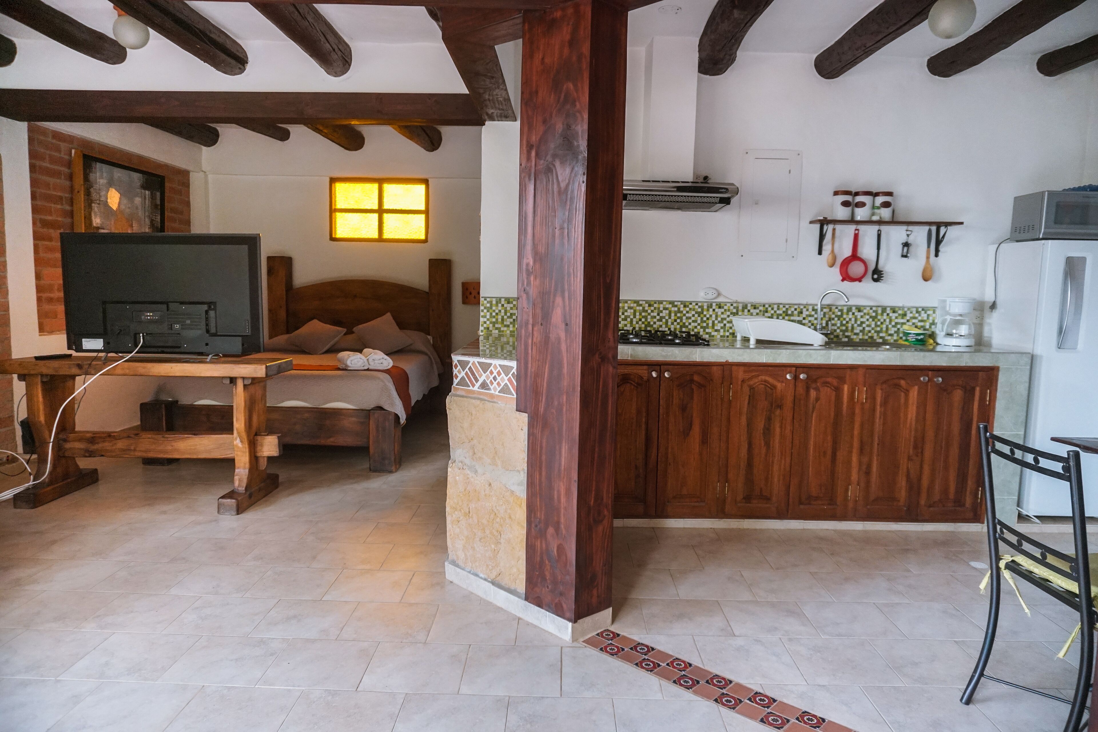 Una habitación acogedora con cama, televisión, mesa de madera y una zona de cocina con armarios y refrigerador.