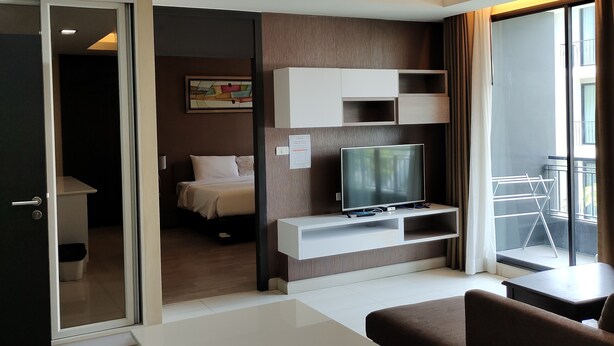 Habitació d'hotel moderna amb televisió de pantalla plana, sofà, taula de menjador, balcó amb estendal i porta corredissa que dona a un dormitori.