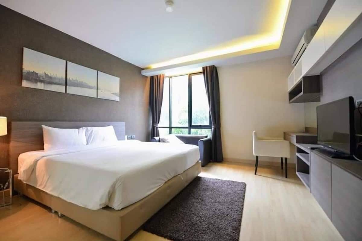 Quarto de hotel moderno com cama grande, escrivaninha, televisão e janela com cortinas.