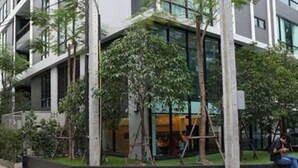 Un edifici modern amb múltiples plantes, grans finestres i una combinació de verdura, incloent arbres i arbustos.