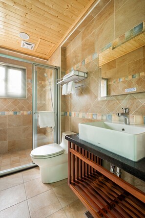 A bathroom with a glass shower enclosure, a white toilet, a sink with a black countertop, and a wooden vanity. - Ediman Bed and Breakfast (Hualien City)