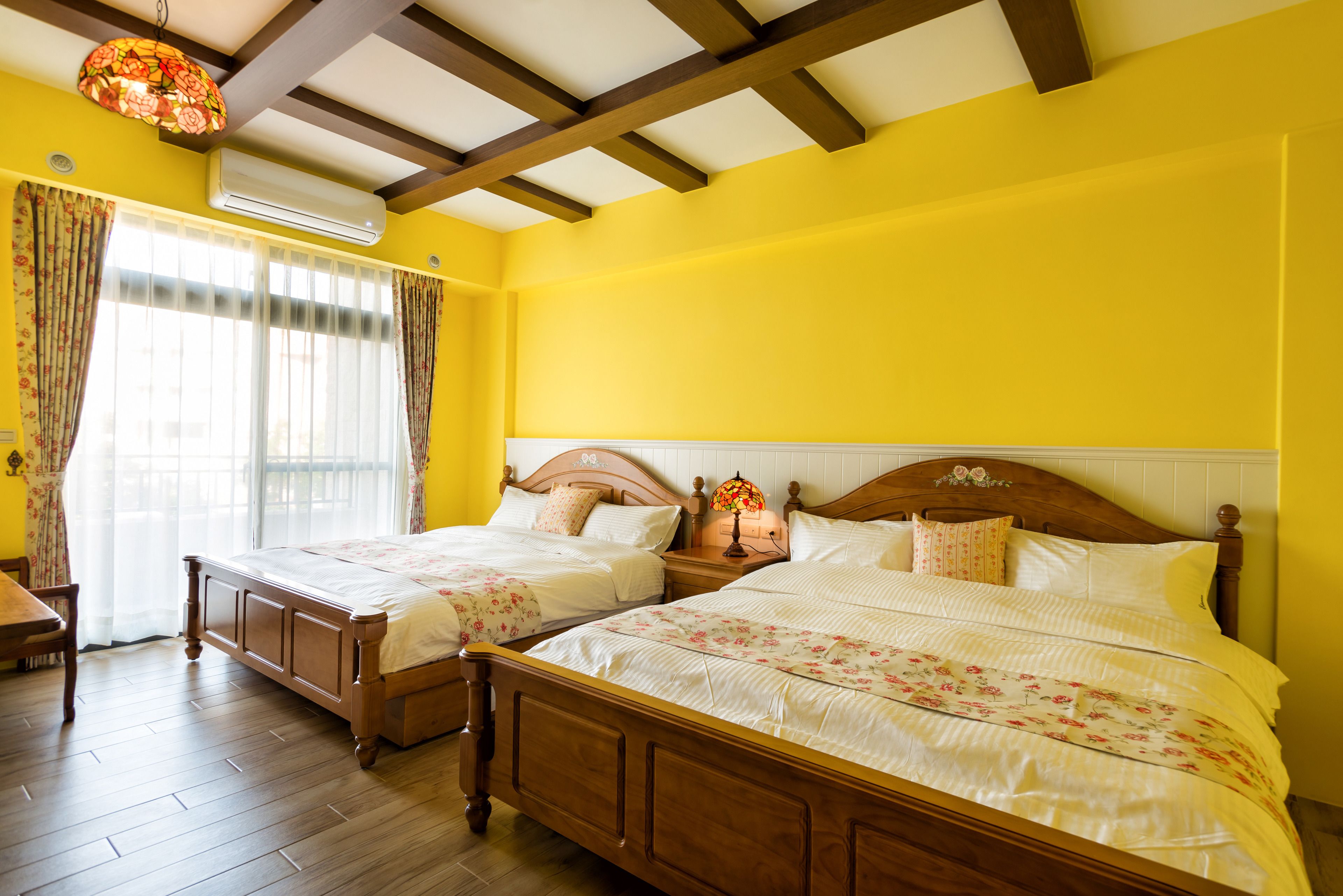 A bedroom with two wooden beds, a wooden floor, a ceiling with exposed beams, and a window with curtains.