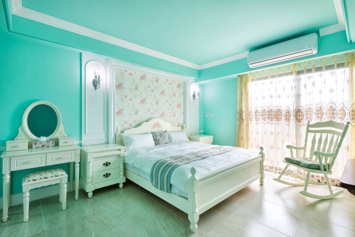 A bedroom with a bed, a dresser, a vanity, a chair, and a window with curtains.