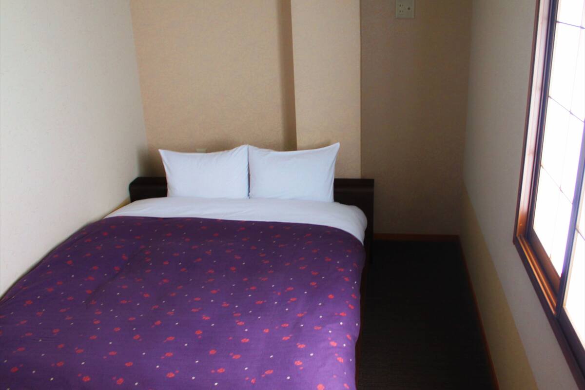 Ett litet hotellrum med en säng, ett fönster och en enkel vägg.