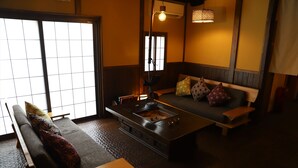 A traditional Japanese-style room with tatami flooring, a low table, a sofa with cushions, and a built-in charcoal grill. - K's House Takayama Oasis - Quality Hostels (Takayama)