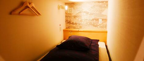 Una habitación pequeña y estrecha con una cama individual, un perchero de madera y una pared con diseño.