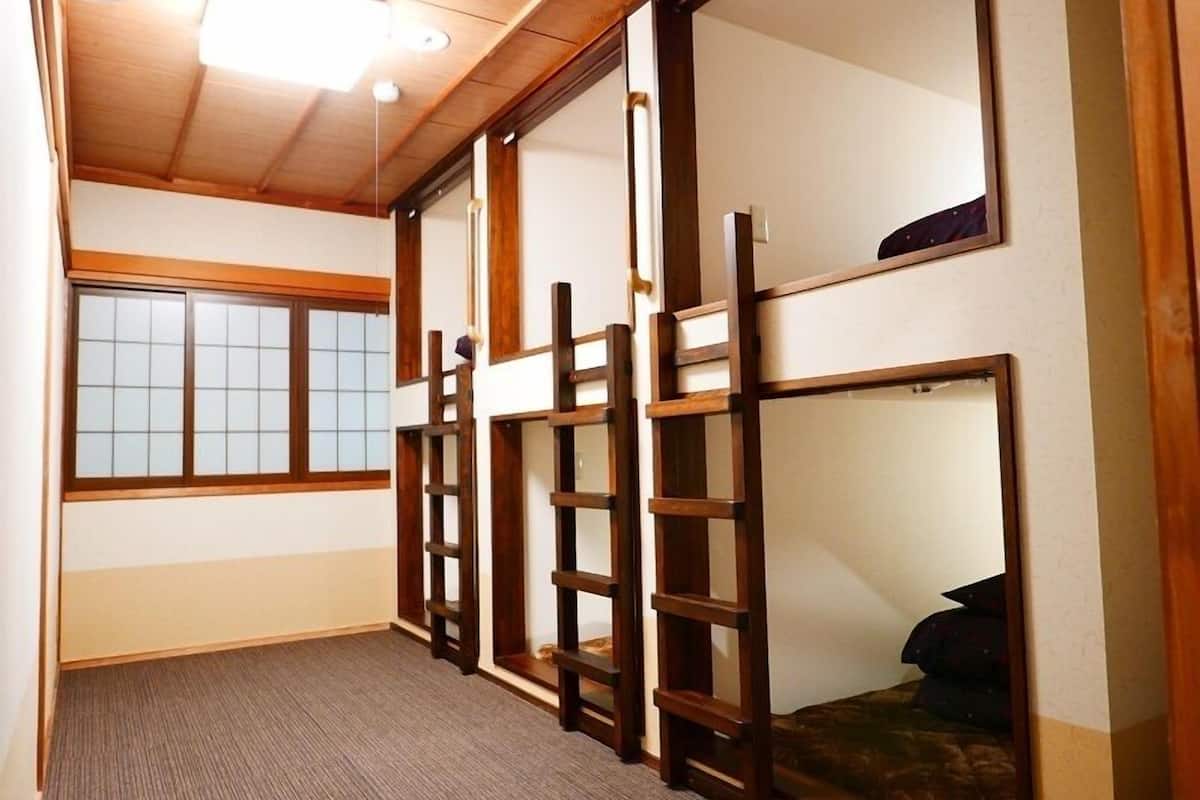 A room with tatami flooring, a sliding door, a bed with a dark cover, and a window with wooden frames.
