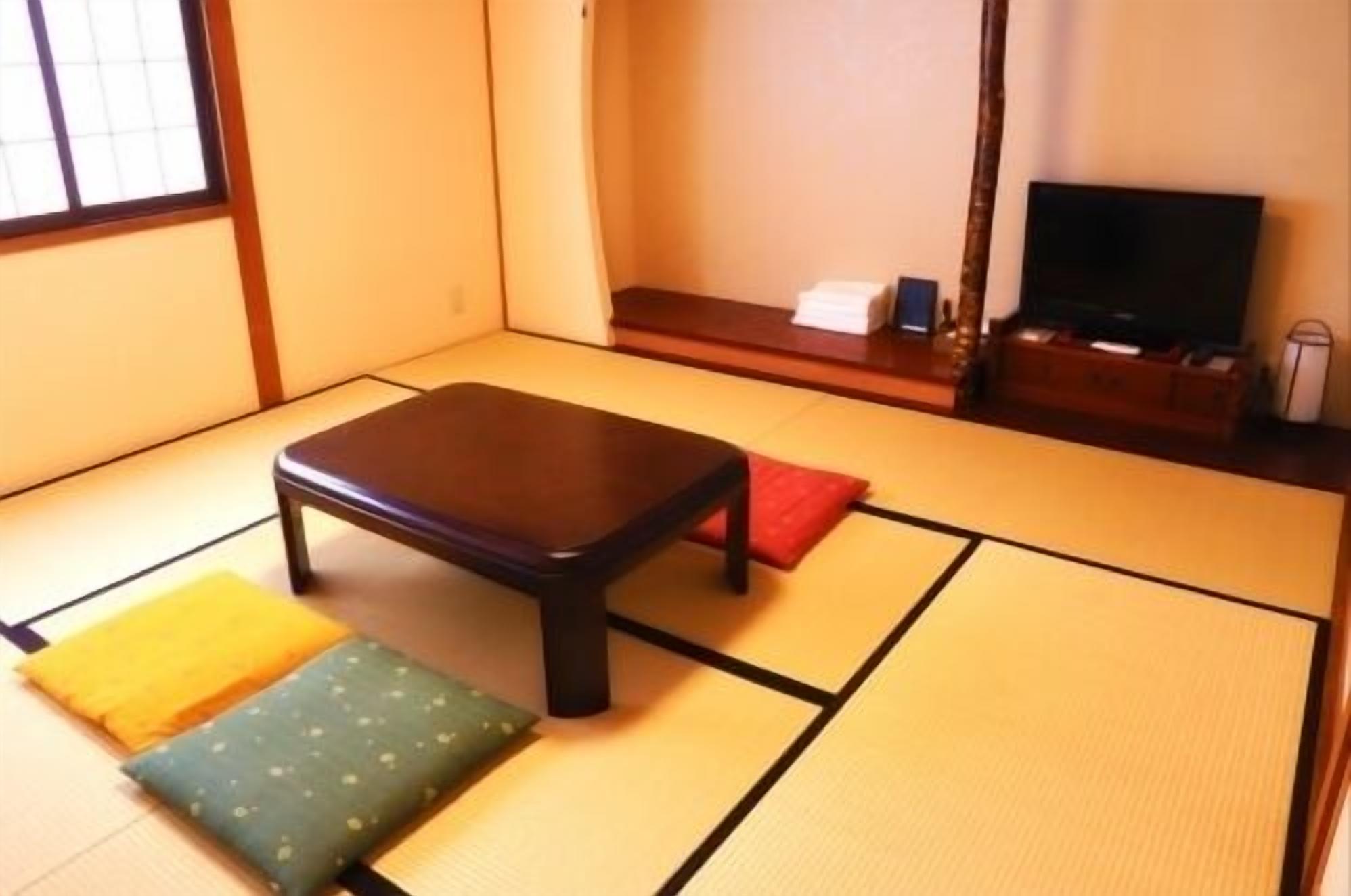 A tatami mat room with a low wooden table, cushions, and a television.