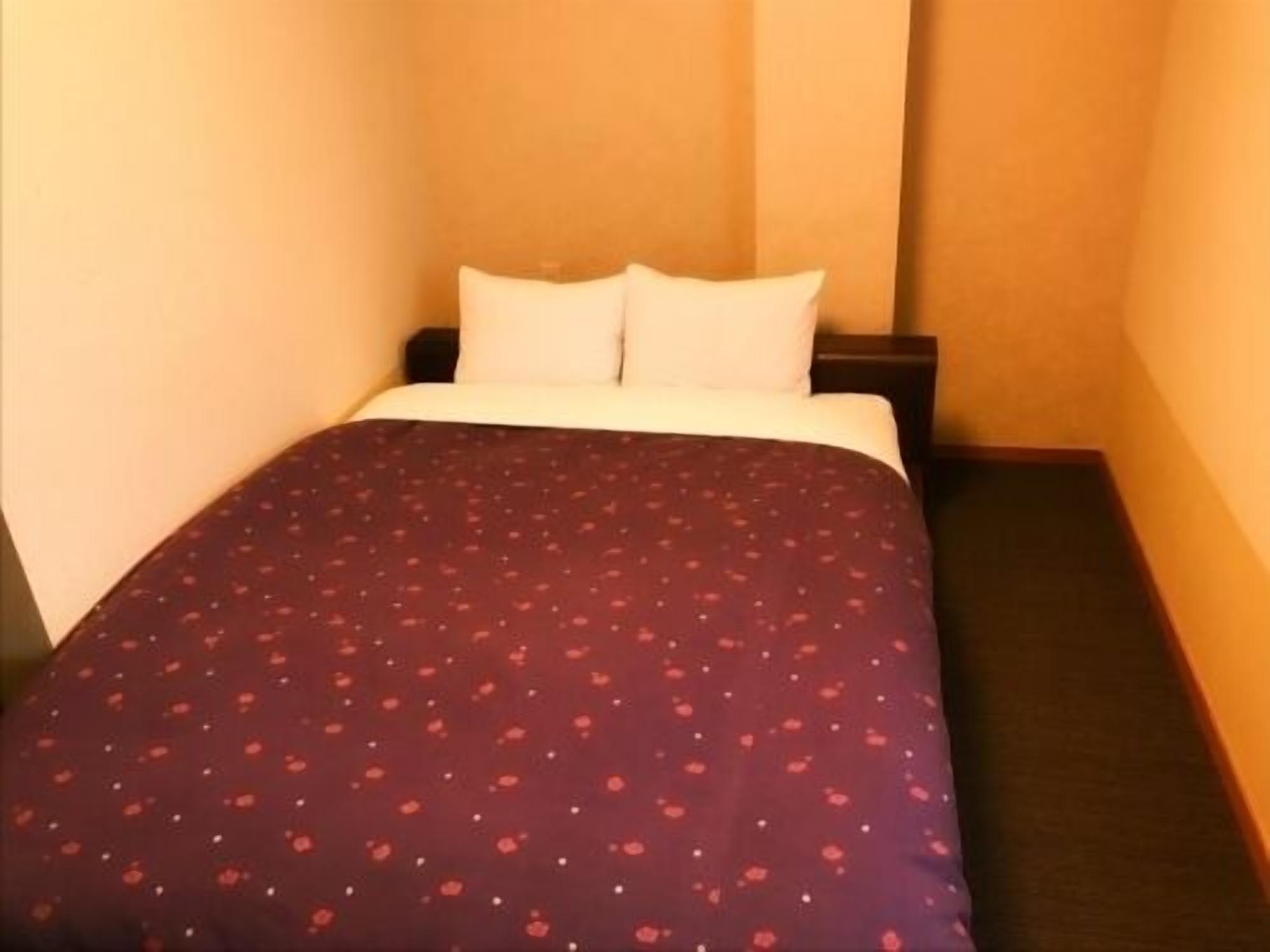 A single bed with a patterned bedspread, a white pillow, and a dark-colored nightstand.