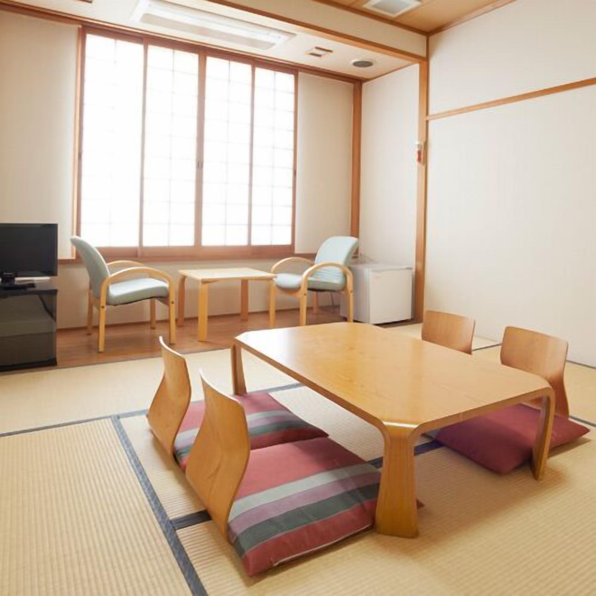 A room with tatami flooring, a low table with cushions, and a television on a stand.