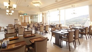 Un vaste espace dédié à la salle à manger, avec de nombreuses tables et chaises, de grandes fenêtres offrant une vue sur la ville et d’élégants lustres.