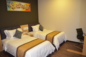 Ein Hotelzimmer mit zwei Betten, jeweils mit weißer Bettwäsche und braunen Akzenten, einem Nachttisch mit Telefon, einem Sessel und einem Bild an der Wand.