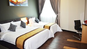 A hotel room with two beds, a desk with a chair, a painting on the wall, and a window with curtains.